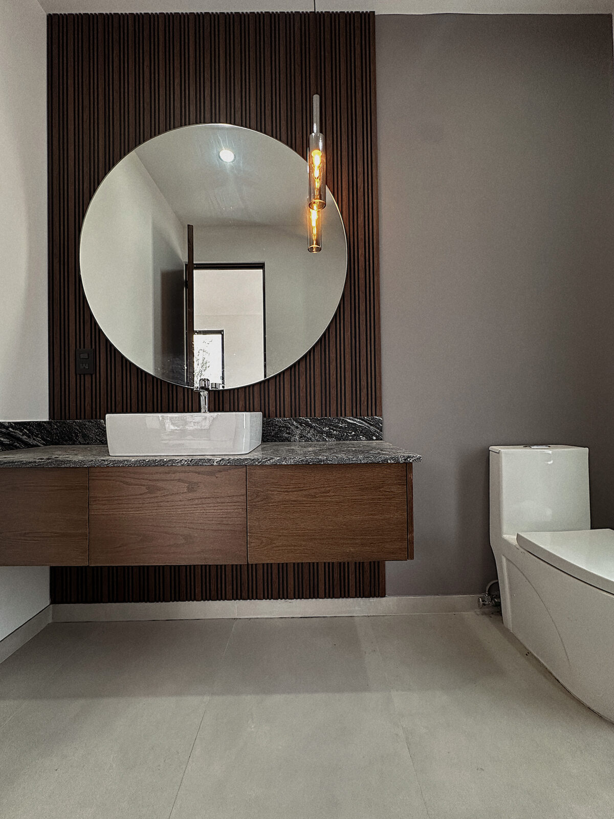 Guest bathroom with wood slat wall and round mirror · Casa Britania, Morelia