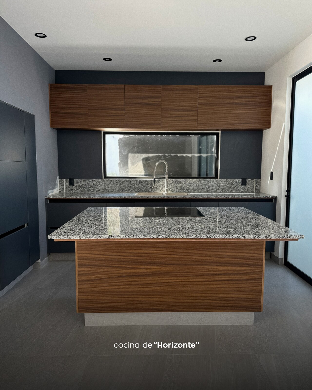 Cocina con isla central de granito gris y gabinetes de madera · Casa Horizonte