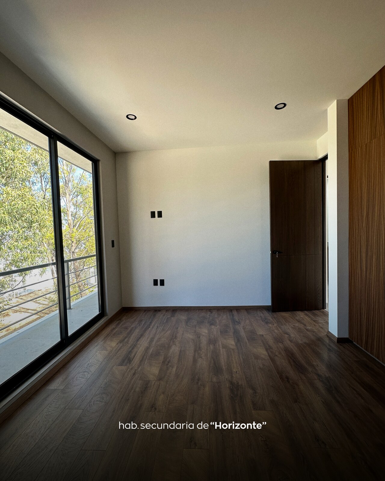 Habitación secundaria con piso de madera oscura y ventanal corredizo · Casa Horizonte